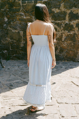 Woman in a light blue dress standing against a stone wall.