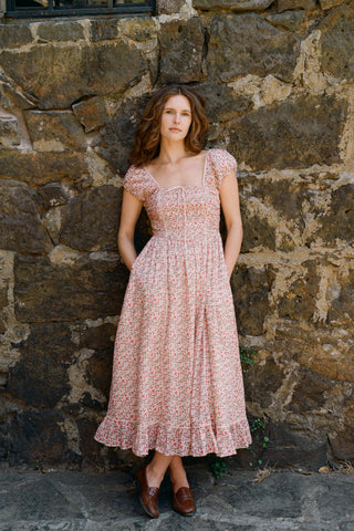 Woman in a floral dress standing against a stone wall