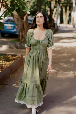 Woman in a green dress standing on a sidewalk with trees and parked cars in the background.