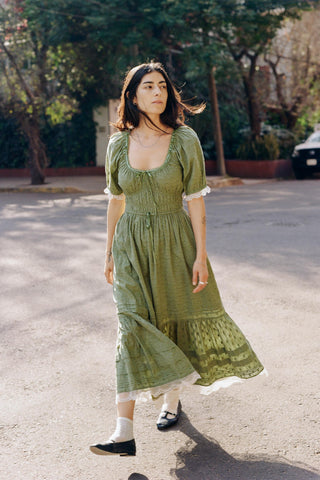 Woman in a green dress standing on a street with trees in the background
