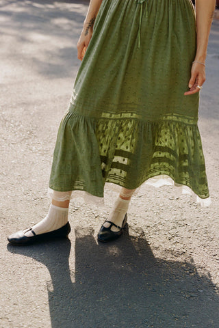 Person wearing a green dress with ruffled hem on a street.
