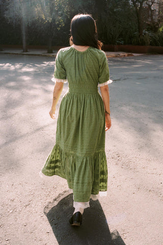 Woman in a green dress walking on a paved path with trees in the background