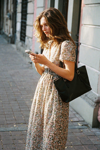 Woman in a green floral dress using a phone on a city street