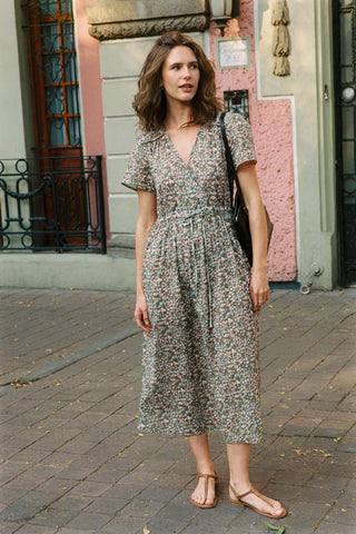 Woman in a green floral dress standing on a street with a building in the background