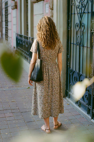 Woman in a green floral dress walking down a sidewalk with a black bag