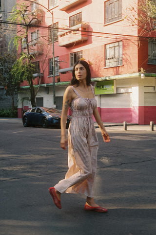 Woman in a long dress walking on a street with a pink building in the background