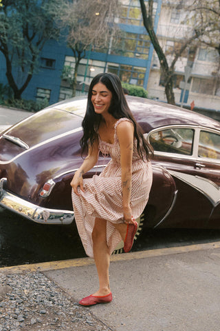 Woman in a dress standing next to a vintage car on a city street.
