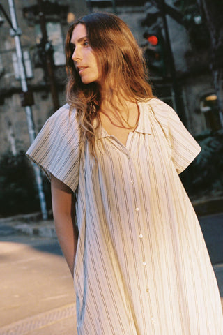 Woman wearing a light-colored dress with ruffled sleeves on a city street.