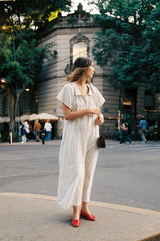 Woman in a white dress standing on a city street with trees and buildings in the background