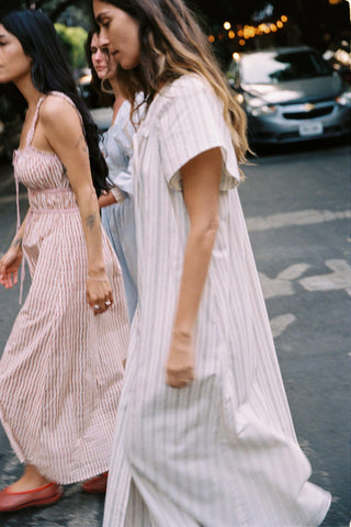 Two women walking on a street, one in a pink dress and the other in a white dress.