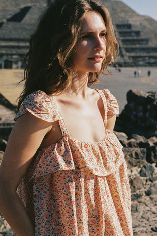 Woman in a floral dress standing in front of a pyramid-like structure.