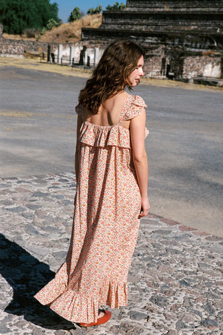 Woman in a floral dress standing on a stone path with ancient architecture in the background