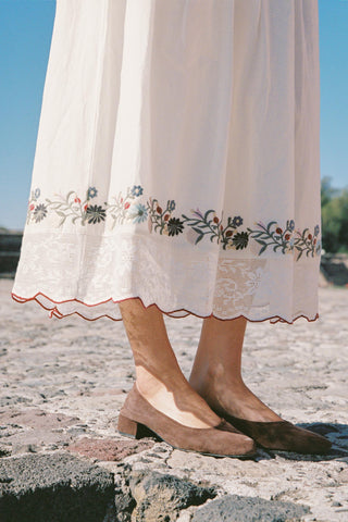 White skirt with floral embroidery and brown shoes on a stone surface.