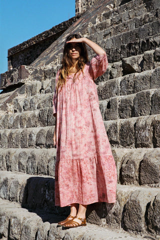 Woman in a pink dress standing on stone steps with a clear blue sky.