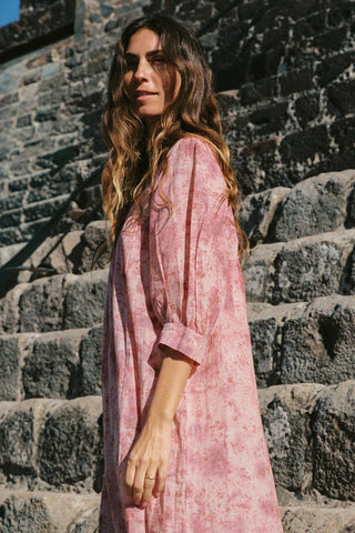 Woman in a pink dress standing on stone steps with a stone wall background