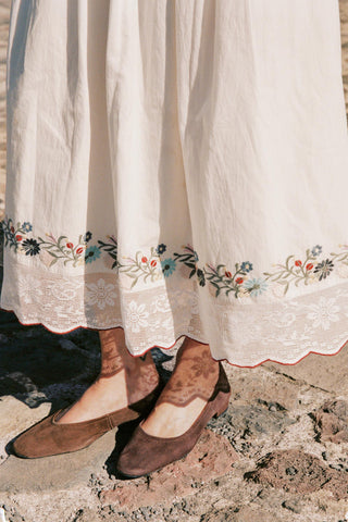 Brown shoes worn with a white skirt featuring floral embroidery on a stone surface