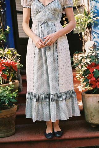 Woman wearing a patterned dress standing among potted plants.