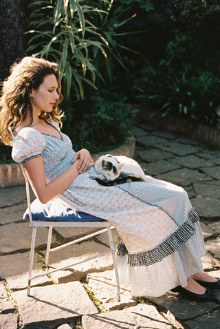 Woman sitting outdoors with a cat on her lap, wearing a light blue dress.