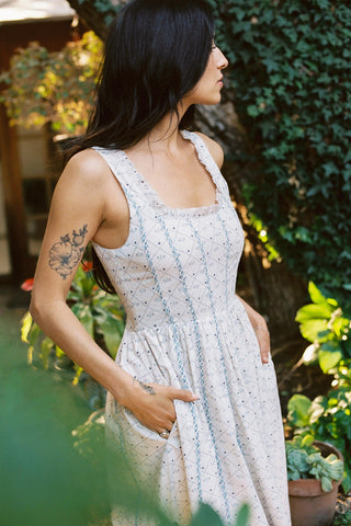 Woman in a light dress standing outdoors with greenery around