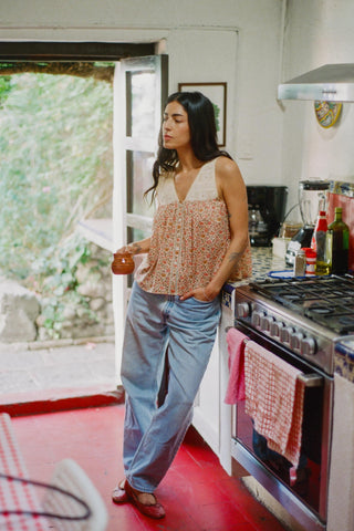 Woman standing in a kitchen with a red floor, wearing a patterned top and jeans.