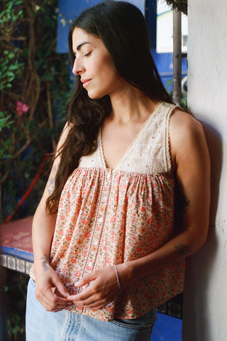 Woman wearing a floral sleeveless top and jeans leaning against a wall.