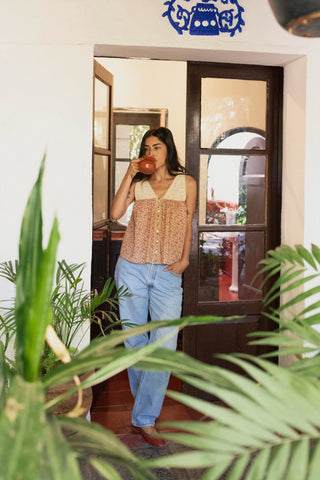 Woman taking a sip from a cup in a home setting with plants in the foreground
