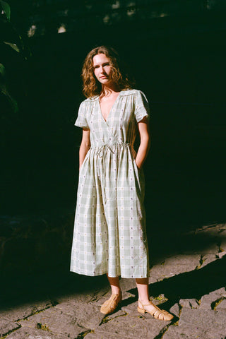 Woman in a green plaid dress standing on a stone path with a dark background