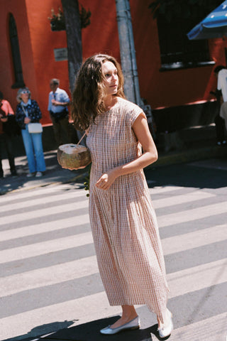 Woman in a long checkered dress walking on a street with a red building in the background.