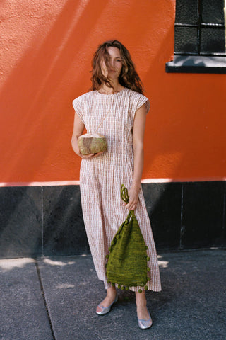 Woman holding a green bag and coconut against an orange wall