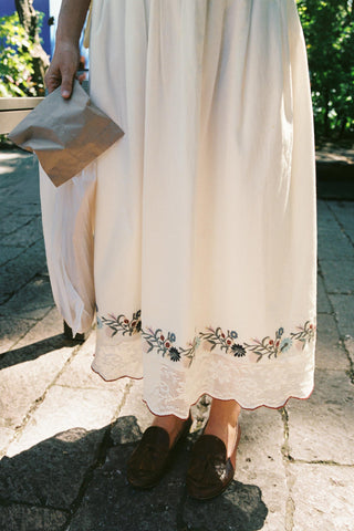 Person wearing a long, light-colored skirt with floral embroidery on a stone path.