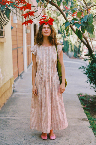 Woman in a long dress standing outdoors with greenery and a building in the background