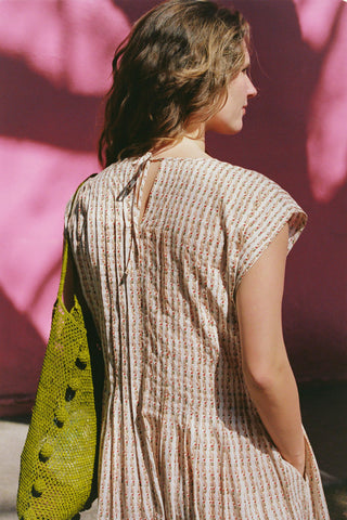 Woman wearing a patterned dress holding a green bag against a pink wall.