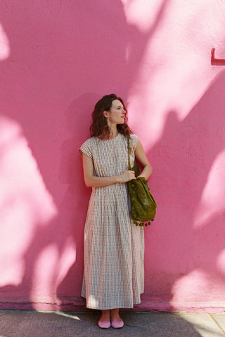 Woman in a checkered dress holding a green bag against a pink wall