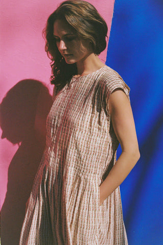 Woman in a patterned dress standing against a pink and blue gradient background