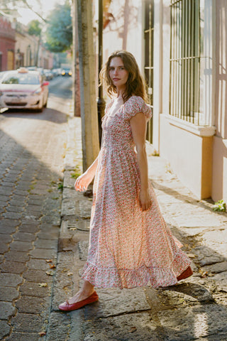 Woman in a floral dress walking on a sunlit street.
