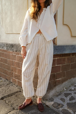 Person wearing a white blouse and striped pants standing against a brick wall.