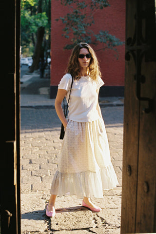 Woman in a patterned skirt standing on a street with a red building in the background