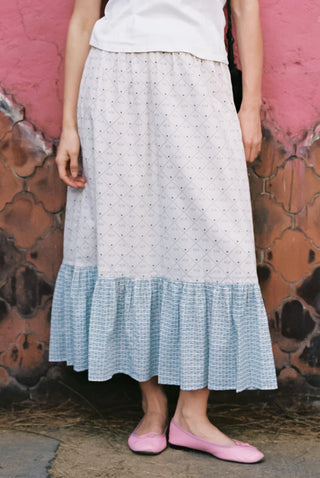 Person wearing a long, patterned skirt with a white top against a textured pink wall.