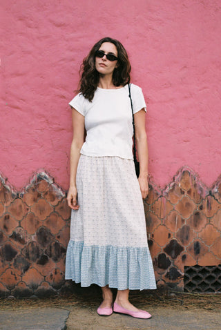 Woman wearing a white top and blue checkered skirt against a pink wall.