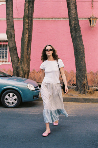 Woman walking on a street with a pink wall and car in the background