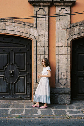 Woman in a patterned skirt standing in front of a stone building with large doors.