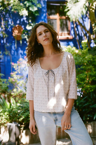 Woman wearing a white blouse with floral patterns and light blue jeans in a garden setting.