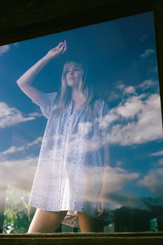 Woman in a white dress standing outdoors with a blue sky and clouds in the background