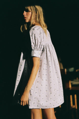 Woman wearing a light purple floral dress against a dark background