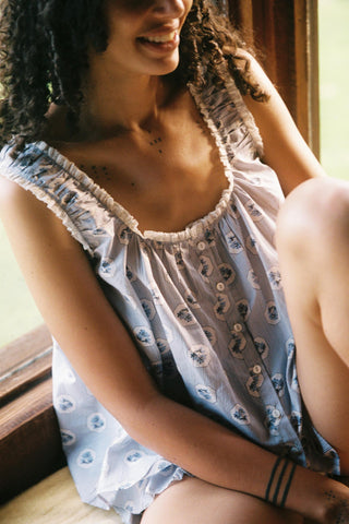 Woman wearing a light blue floral set sitting by a window.