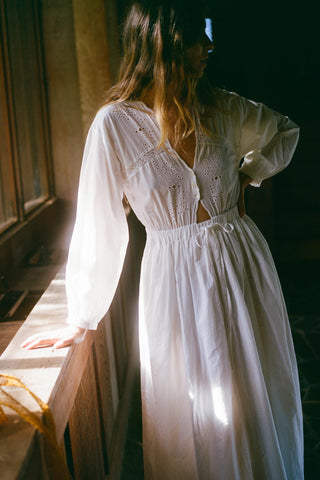 Woman wearing a white dress with long sleeves in a softly lit room.