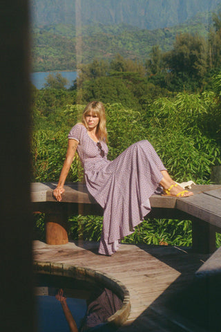 Woman in a purple dress sitting on a wooden bench with a scenic background