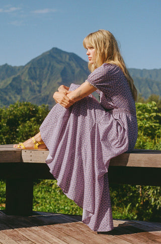 Woman in a purple dress sitting on a wooden bench with mountains in the background