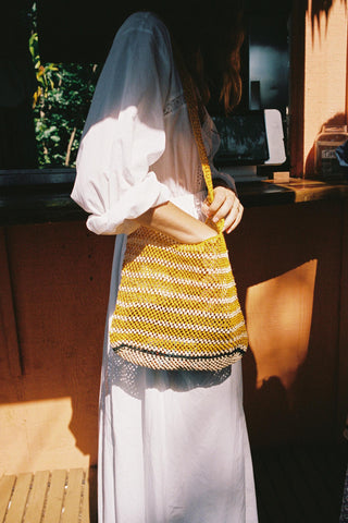 Person wearing a white dress with a yellow and white striped woven bag