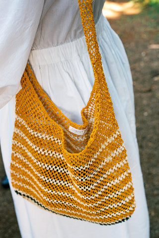 Yellow and white striped handbag held by a person wearing a white dress.